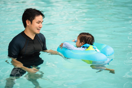 happy father with toddler baby girl playing in an inflatable ring in the swimming poolの写真素材
