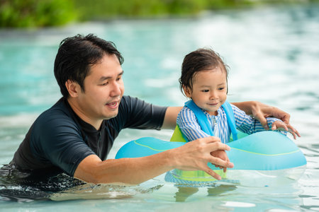 happy father with toddler baby girl playing in an inflatable ring in the swimming poolの写真素材