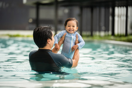 father holding and lifting todler baby in his arms while playing water in a swimming poolの写真素材