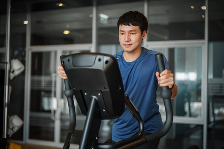 young man doing exercise on an elliptical cross trainer in sport fitness gym