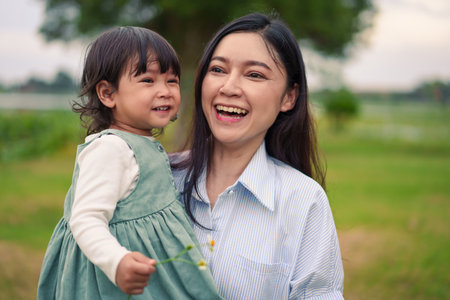 happy mother holding toddler baby girl on grass field in the parkの写真素材