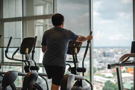 young man doing exercise on an elliptical cross trainer in sport fitness gymの写真素材