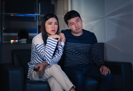 bored couple watching TV on a sofa at nightの写真素材