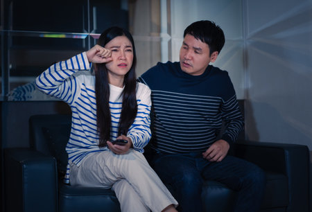 crying couple watching romantic movie TV on a sofa at nightの写真素材