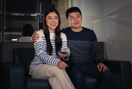 happy couple watching TV on a sofa at nightの写真素材