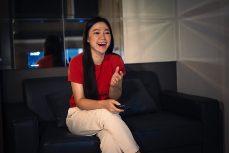 funny woman watching TV on a sofa at nightの写真素材