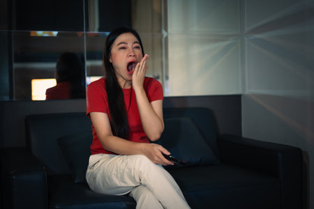 sleepy woman yawning while watching TV movie on a sofa at nightの写真素材