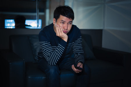 bored man watching TV on a sofa at nightの写真素材