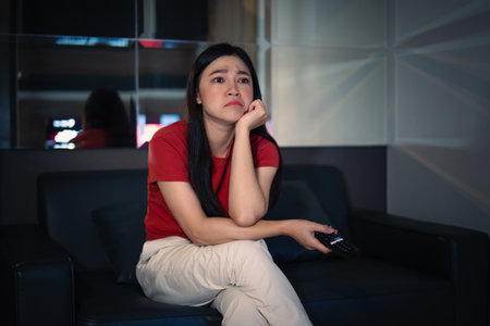 bored young woman watching TV on a sofa at nightの写真素材