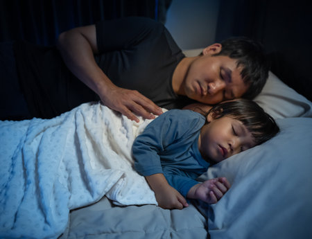 father embraces the toddler baby sleeping together in a bed at nightの写真素材