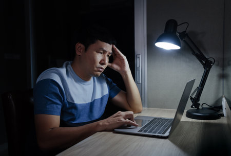 stressed man headache while working with laptop at a nightの写真素材