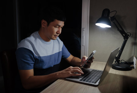man woking with smartphone and laptop at a nightの写真素材