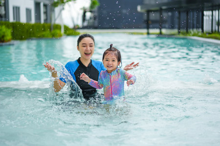 happy mother with her toddler baby girl playing water splashing in a swimming poolの写真素材