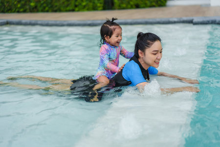 happy mother giving piggyback ride to toddler baby girl in a swimming poolの写真素材