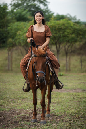 happy woman riding brown horse on meadow fieldの写真素材