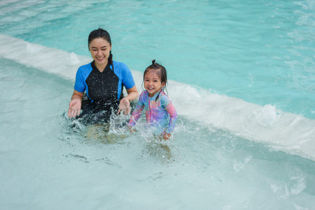 happy mother with her toddler baby girl playing water splashing in a swimming poolの写真素材
