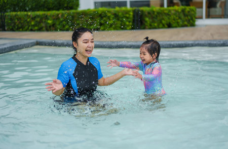 happy mother with her toddler baby girl playing water splashing in a swimming poolの写真素材
