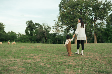 happy mother walking with her toddler baby girl on a grass fieldの写真素材