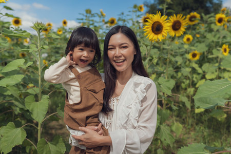 cheerful mother holding her toddler girl in sunflower field. happy family conceptの写真素材