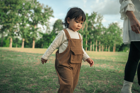 toddler baby girl walking with her mother in a grass fieldの写真素材