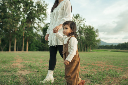 little toddler baby girl holding her mother's hand and walking in a grass fieldの写真素材