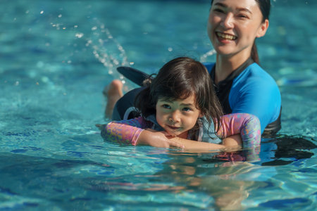 mother teaching toddler baby girl swimming in the pool and wearing life jacketの写真素材