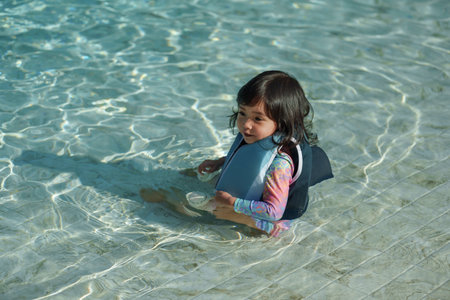happy toddler baby girl in life jacket playing water in the swimming poolの写真素材