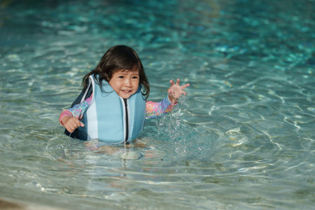 happy toddler baby girl in life jacket playing water splashing in the swimming poolの写真素材