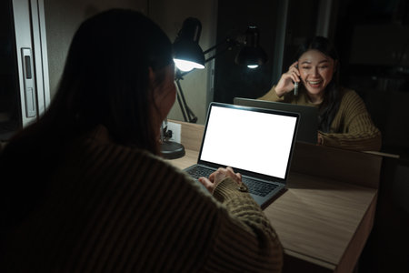 happy woman talking with smartphone while working with laptop at a night (with clipping path)の写真素材