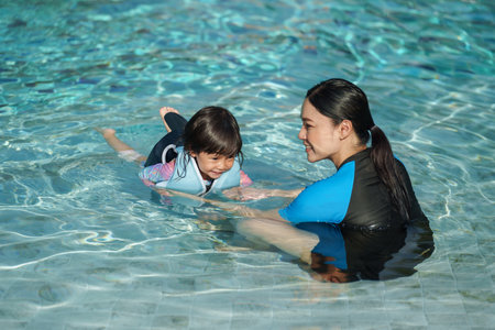 mother teaching toddler baby girl swimming in the pool and wearing life jacketの写真素材