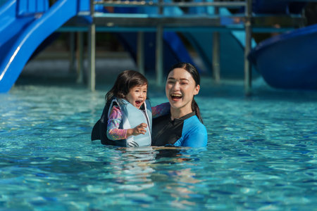 happy mother with toddler baby girl in life jacket playing in the swimming poolの写真素材