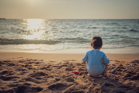 toddler baby girl playing sand toy on the sea beach at sunset in Pattaya, Thailandの写真素材