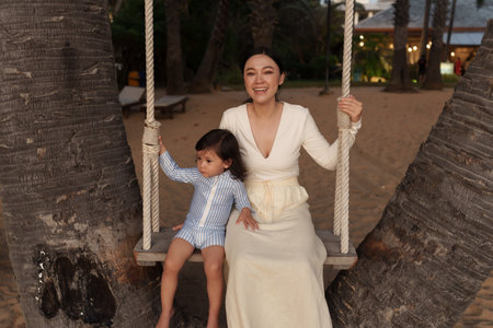 happy mother and toddler baby girl ride on wood swing on the sea beach in Pattaya, Thailandの写真素材