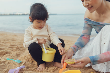 happy toddler baby girl playing sand toy with mother on the sea beach in Pattaya, Thailandの写真素材