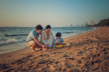 toddler baby girl playing sand toy with father and mother. happy family on the sea beach at sunset in Pattaya, Thailandの写真素材
