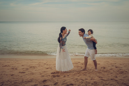 toddler baby girl with parent for piggyback and playing on the sea beach in Pattaya, Thailand. happy family conceptの写真素材
