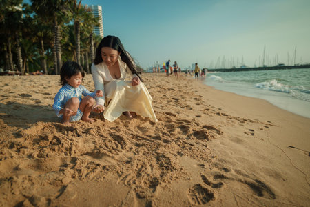 happy toddler baby girl playing sand with mother on the sea beach in Pattaya, Thailandの写真素材