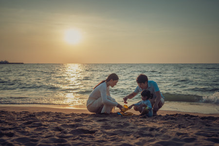 toddler baby girl playing sand toy with father and mother. happy family on the sea beach at sunset in Pattaya, Thailandの写真素材