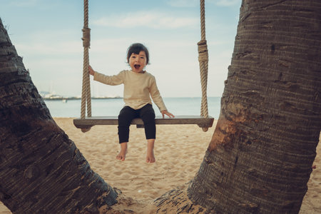 cheerful toddler baby girl ride on wood swing on the sea beach in Pattaya, Thailandの写真素材