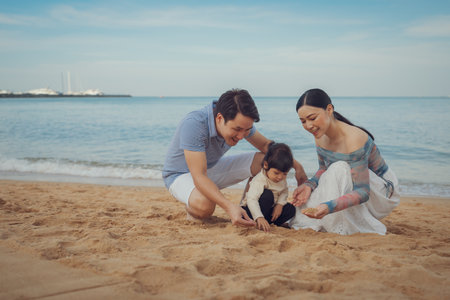 toddler baby girl playing sand with father and mother. happy family on the sea beach in Pattaya, Thailandの写真素材