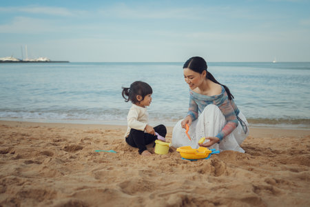 happy toddler baby girl playing sand toy with mother on the sea beach in Pattaya, Thailandの写真素材