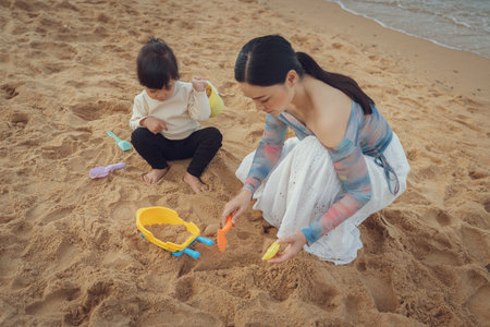 happy toddler baby girl playing sand toy with mother on the sea beach in Pattaya, Thailandの写真素材
