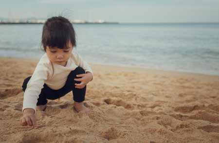 toddler baby girl playing sand on the sea beach in Pattaya, Thailandの写真素材