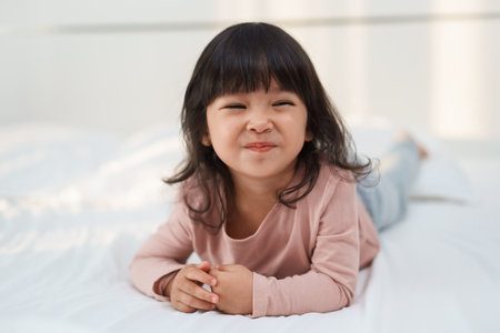 happy toddler girl smiling on a bedの写真素材