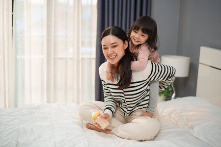 toddler baby girl on a piggy back ride with her mother on a bedの写真素材