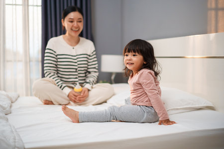 happy toddler baby girl with her mother on a bedの写真素材