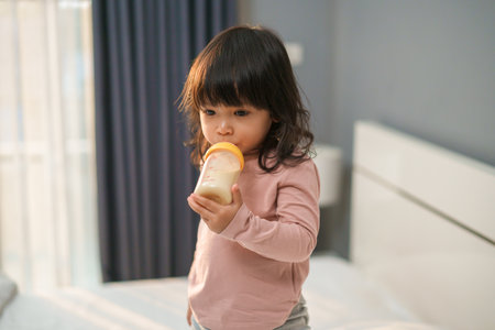 toddler girl drinking milk from bottle on a bedの写真素材