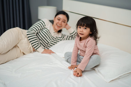 happy toddler baby girl with her mother on a bedの写真素材