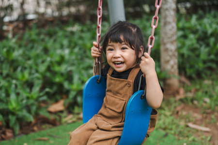 cheerful toddler girl playing on a swingの写真素材