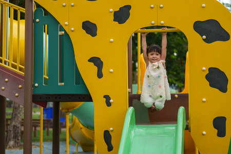 happy toddler girl hanging the yellow bar by her hand at outdoor playground in the park
